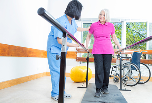 Nurse in blue scrubs assisting elderly woman with physical therapy