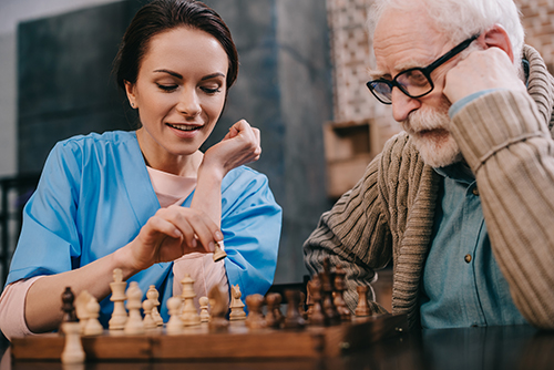 Nurse in blue scrubs playing a game of chess with elderly man