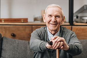 Elderly man sitting on couch with hands resting on his cane smiling